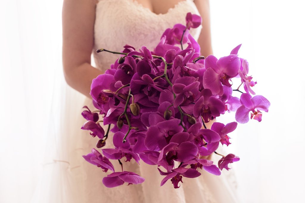 In questa foto le mani di una sposa che nel giorno del suo matrimonio tiene un bouquet di orchidee viola