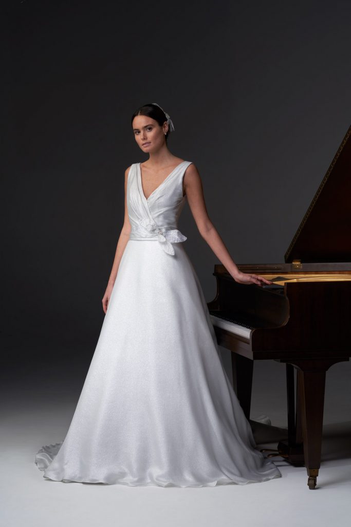 In questa foto una modella vicino ad un pianoforte indossa un abito da sposa Chiara Vitale 2021