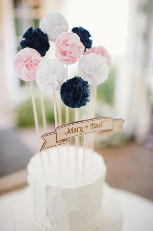 In questa foto una cake topper semplicissimo, realizzato con una targa in legno con su incisi i nomi degli sposi e alcuni pompom di carta colorata