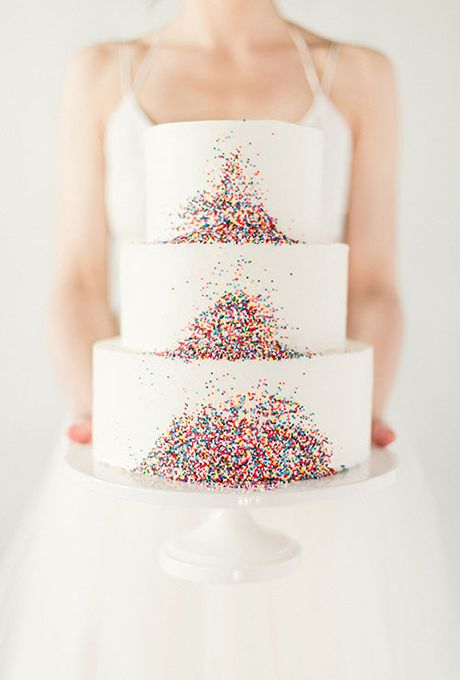 In questa foto una sposa tiene in mano una torta nuziale decorata con confetti colorati