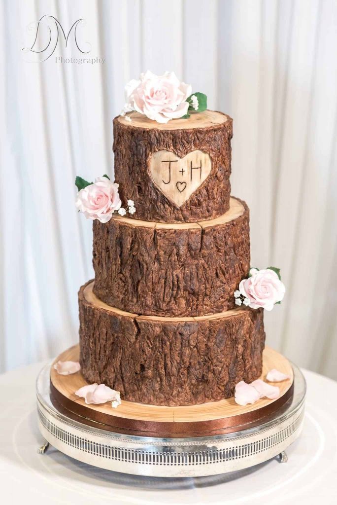 In questa foto una torta matrimoniale che sembra una corteccia d'albero con su inciso un cuore e le iniziali degli sposi