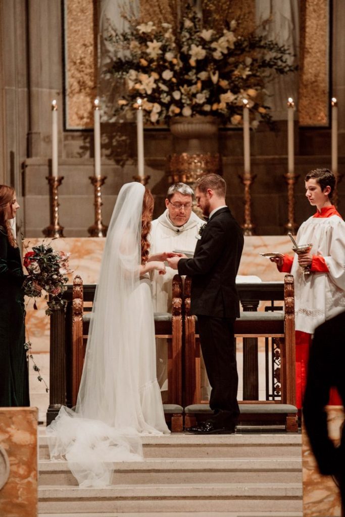 In questa foto due sposi all'altare si tengono per mano scambiandosi le promesse di nozze durante una cerimonia religiosa in chiesa