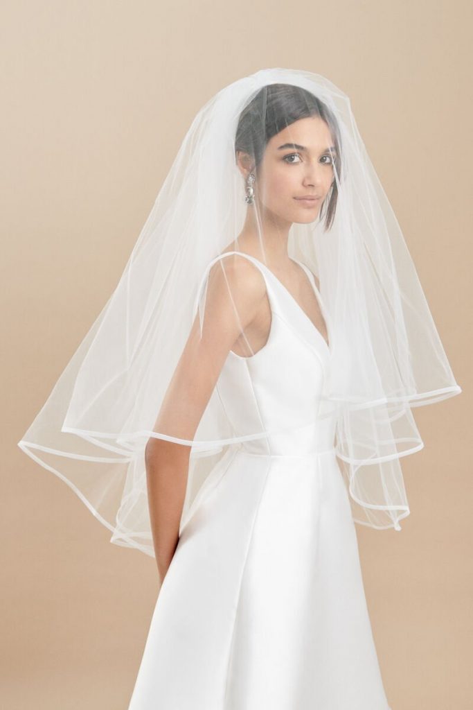 In questa foto una modella indossa un velo da sposa alla vita in tulle con bordo in raso e con calata