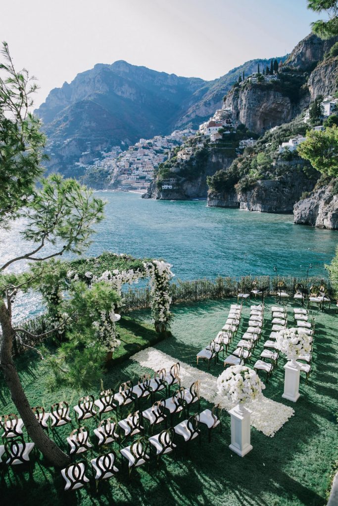 In questa foto l'allestimento di un matrimonio civile su un prato sul lago visto dall'alto.  Alla fine del semicerchio di sedie per gli ospiti è posto un gazebo interamente ricoperto di foglie e fiori bianchi