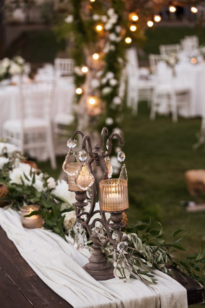 In questa foto il dettaglio della decorazione del tavolo degli sposi con un candelabro in ottone, cristalli pendenti e, attorno, rametti d'ulivo su un drappo di velluto