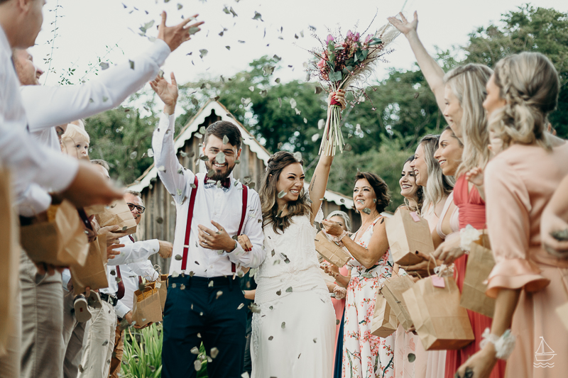 In questa foto due sposi felici attraversano il corridoio della location del matrimonio civili mentre gli invitati lanciano petali e foglie 