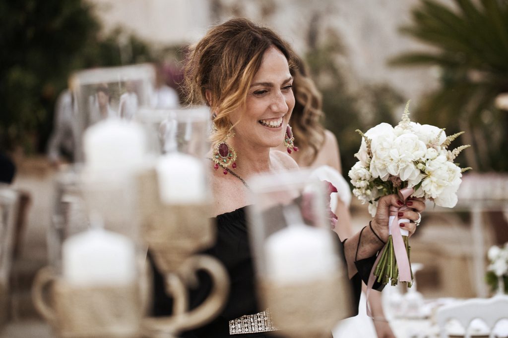 In questa foto la Wedding Planner di Palermo Antonella Candido mentre sorride con il bouquet della sposa in mano dietro ad un candelabro dorato