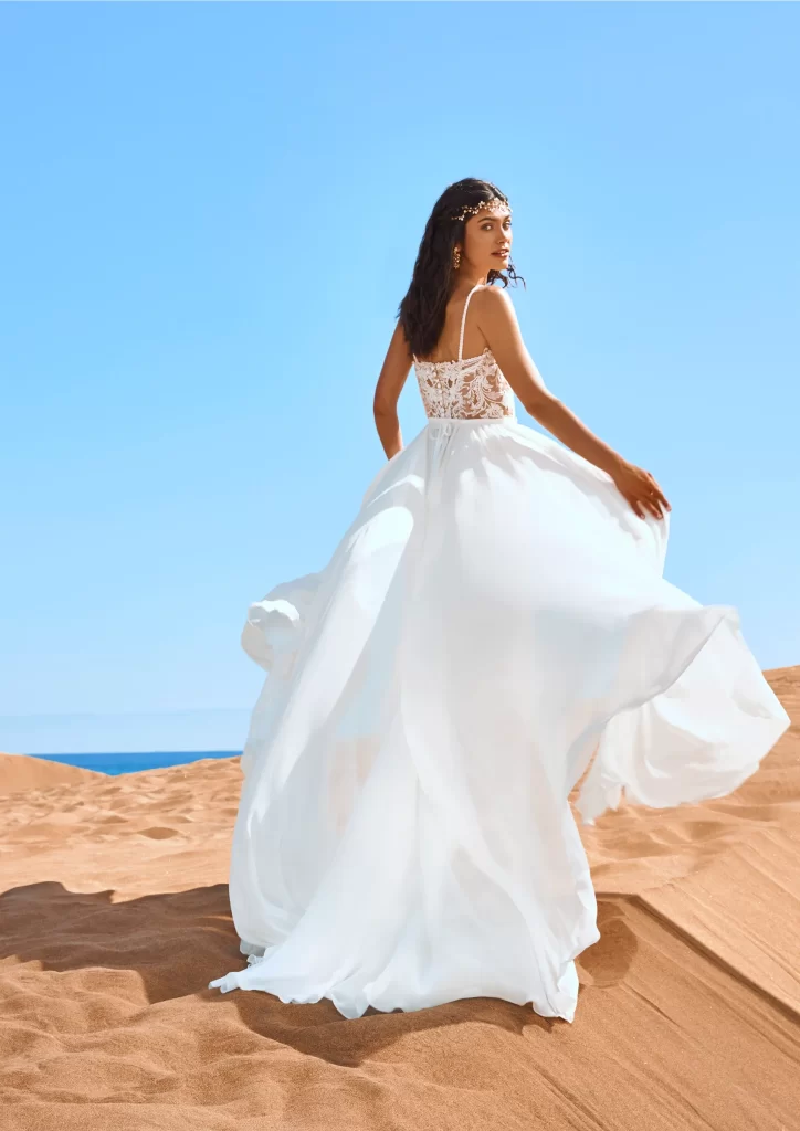 In questa foto una modella indossa un abito da sposa schiena scollata 2022 della collezione Pronovias con scollo di pizzo.