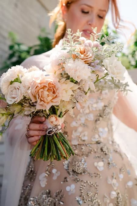 In questa foto, una sposa tiene in mano un bouquet scomposto con fiori dai colori tenui, arricchito nell'impugnatura da due spille antiche