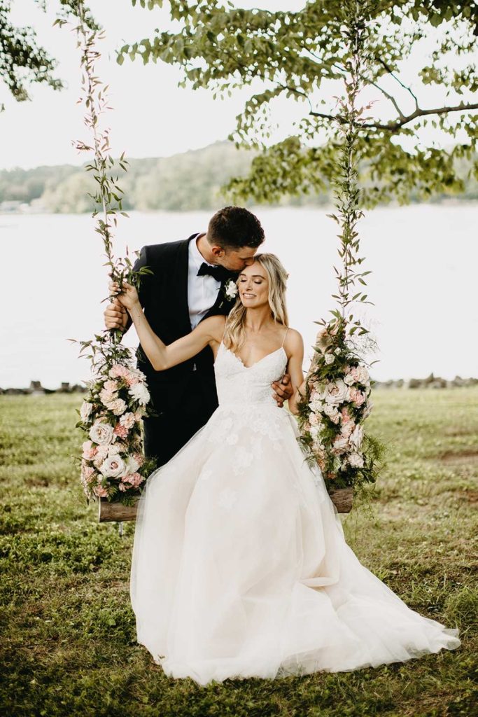 In questa foto due sposi seduti su un'altalena a bordo di un decorata con fiori colore bianco e rosa