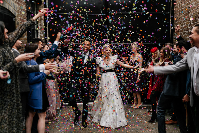 In questa foto idee matrimonio per l'uscita dalla chiesa: due sposi sorridenti camminano tra i coriandoli colorati lanciati dagli invitati