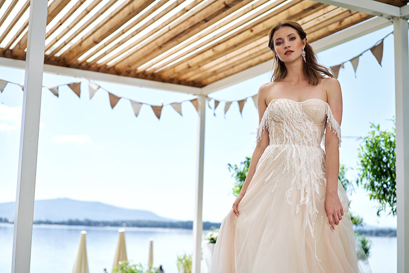 In questa foto una modella indossa un abito da sposa Annais Bridal 2023 in tulle colore avorio, manichette con perline e ramage astratto prezioso su corpetto e punto vita