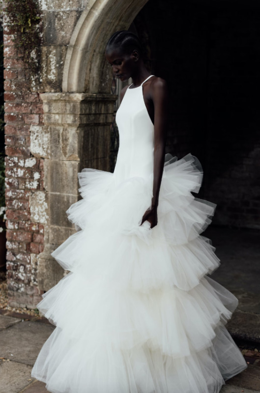 In questa foto la modella posa con un abito da sposa con maxi ruches della collezione Halfpenny London 2023