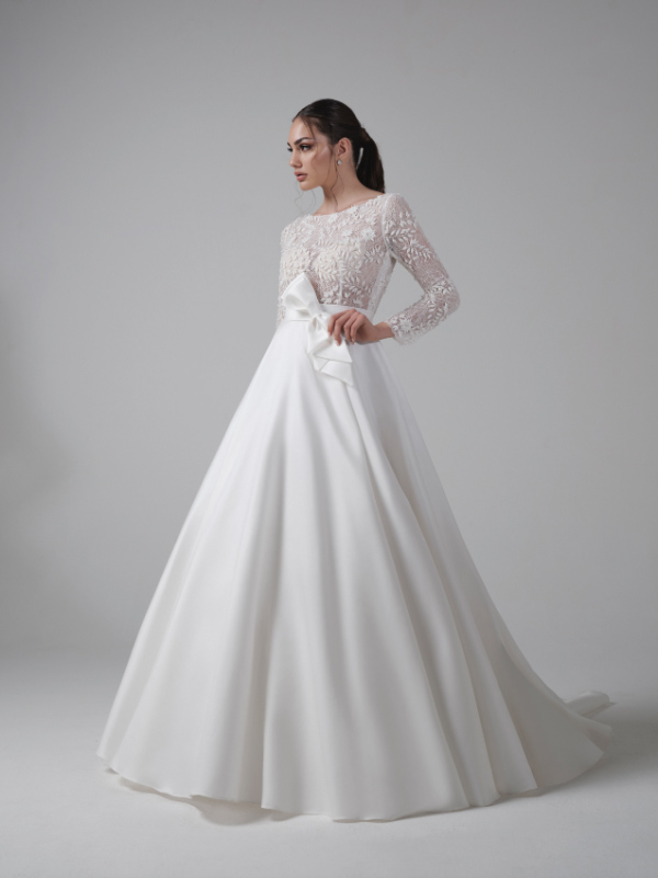 In questa foto una modella indossa un romantico vestito dalla linea ad A della collezione sposa Musa Bridal 2023