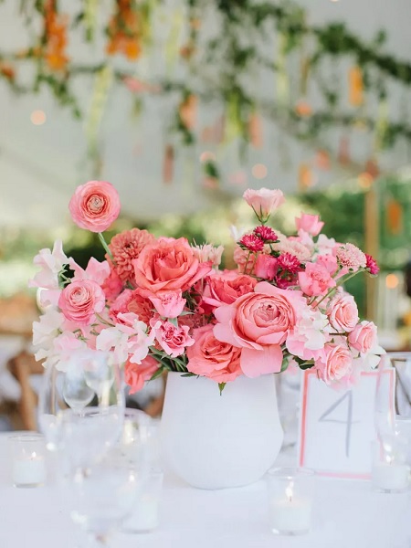 In questa foto, un centrotavola realizzato con un mix di fiori rosa brillante, colore della Biodiversità di Pantone, sistemati all'interno di un vaso bianco 