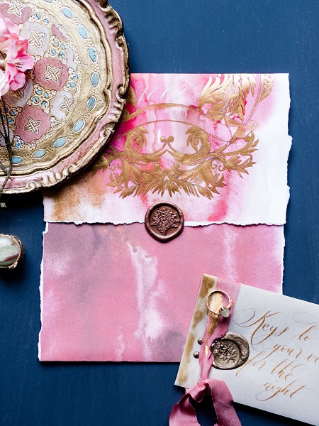 In questa foto, una partecipazione matrimonio chiusa, con busta in rosa brillante, dettagli dorati e sigillo di ceralacca color rame 