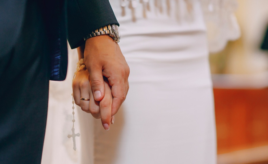 In questa foto le mani di due sposi unite, mentre stringono un rosario durante la celebrazione del loro matrimonio religioso in chiesa