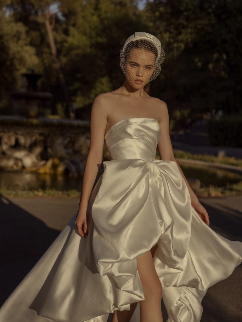 In questa immagine un abito da sposa corto davanti e lungo dietro della collezione 2023 del brand.