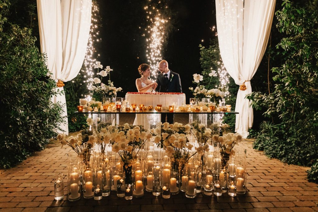 In questa foto Mariavittoria e Claudio durante il taglio della torta: allestimento glamour sui toni dell'oro e del bianco su un imponente tavolo di vetro