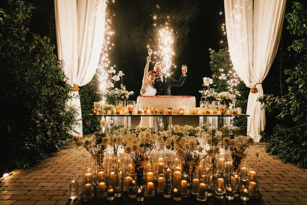 In questa foto Mariavittoria e Claudio durante il taglio della torta: allestimento glamour sui toni dell'oro e del bianco su un imponente tavolo di vetro