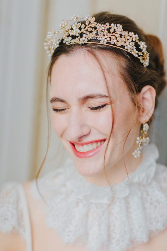 In questa foto il primo piano di una sposa che sorride ad occhi chiusi e che indossa un diadema di perle e oro e orecchini pendenti abbinati