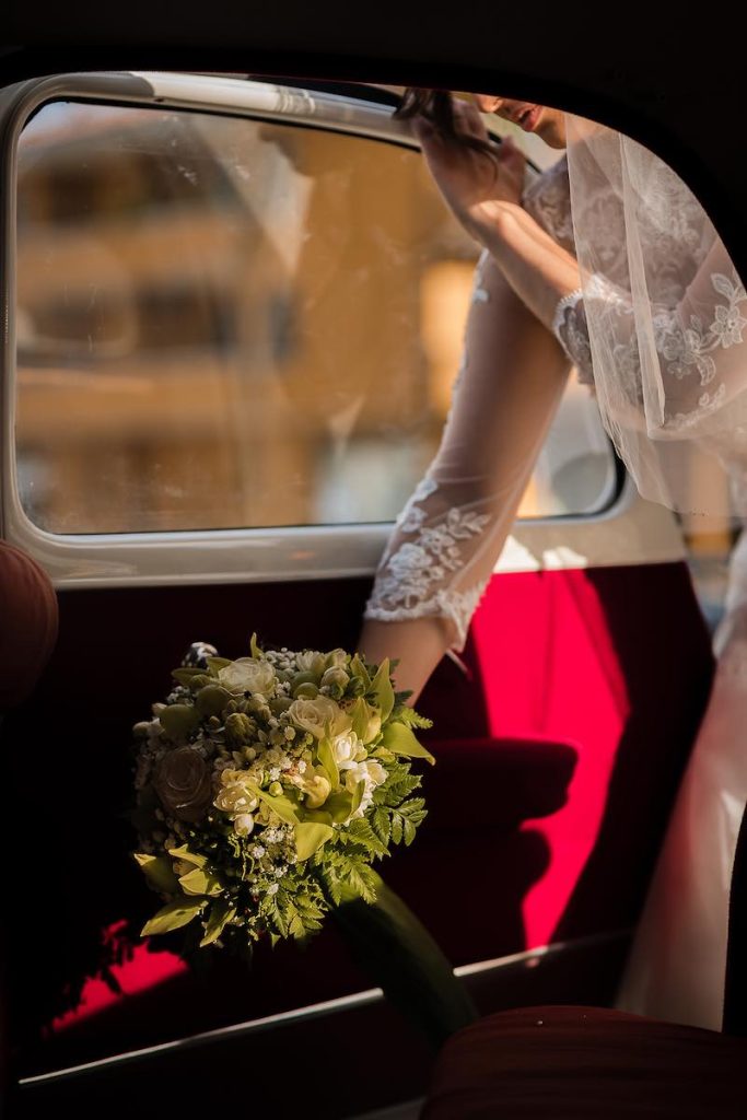 In questa foto di Nicola Tanzella il dettaglio del bouquet di mughetto di una sposa che entra in una macchina di colore rosso