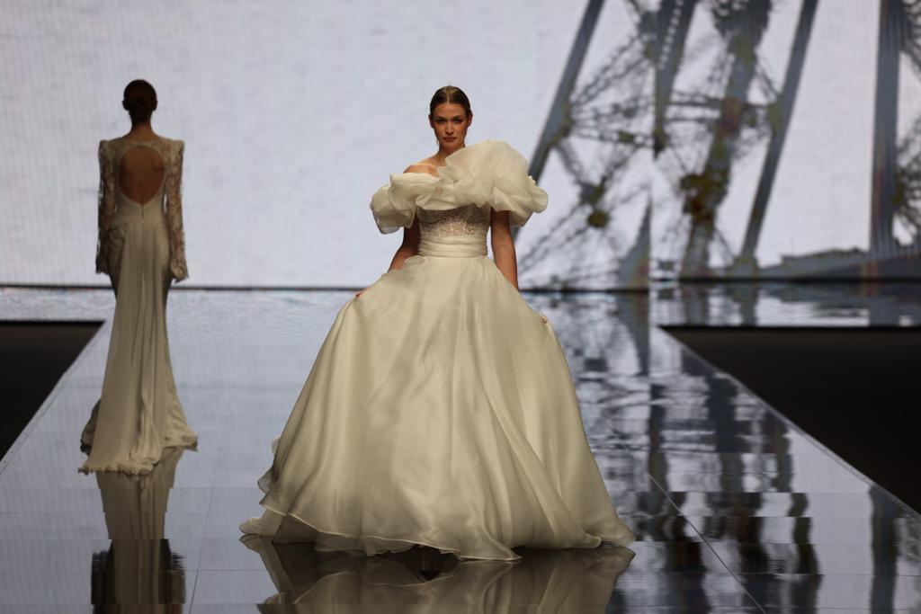 In questa foto una modella sfila indossando un abito da sposa Michela Ferriero 2024 dalla linea ad A in organza di seta con ruches over lungo la scollatura a barca