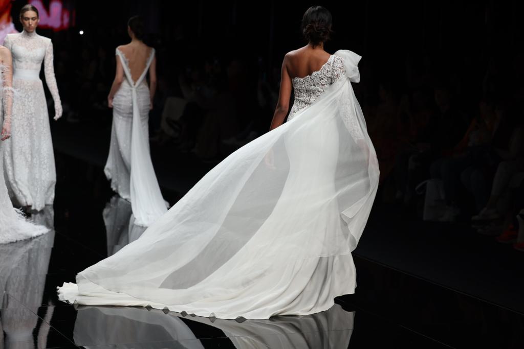 In questa foto una modella di spalle indossando un abito da sposa Michela Ferriero 2024 mezza sirena con ampia manica in chiffon fermata da un maxi fiocco sulla spalla