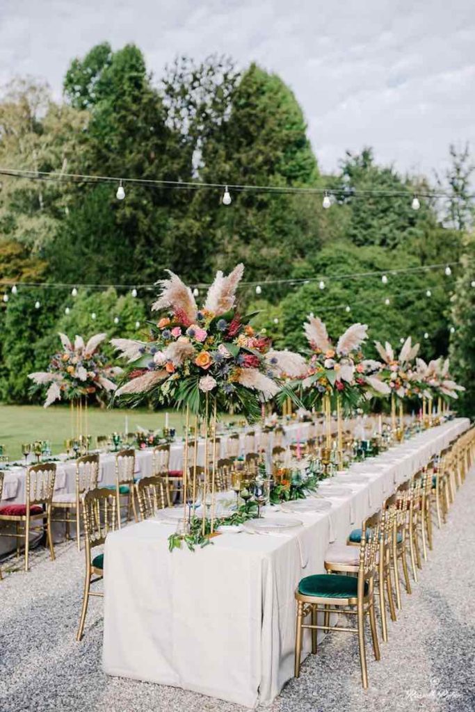 In questa foto uno degli allestimenti matrimoni di Idee da Sogno: una tavola decorata con composizioni e altate di pampas e fiori di colore e rosso e rosa