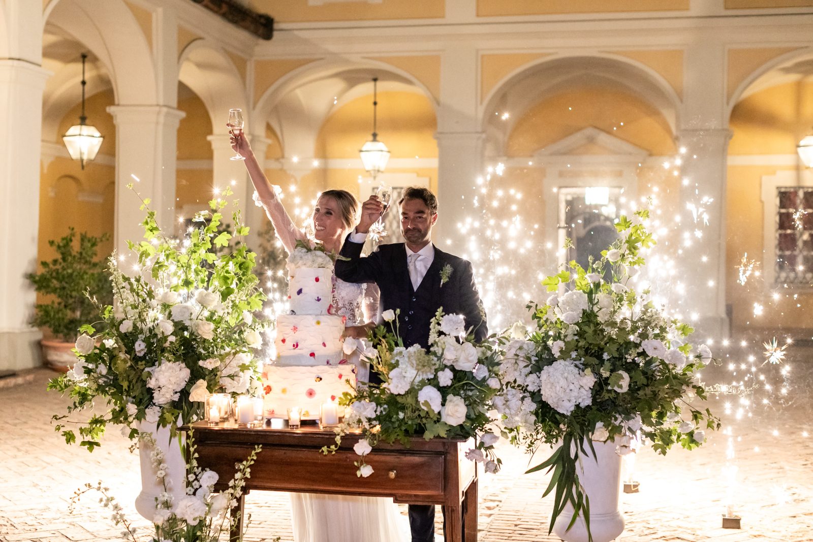 In questa foto due sposi festeggiano davanti al tavolo della torta nuziale realizzati dal catering Da Petti