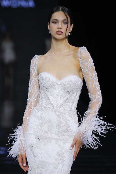 In questa foto una modella sfila sulla passerella della Barcelona Bridal Fashion Week 2023 mentre indossa un abito da sposa Wonà Concept 2024 con effetti plumage sui polsi delle maniche
