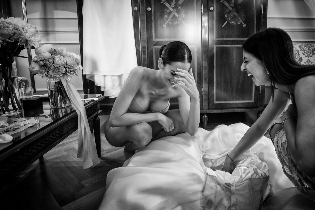 In questa foto Beatrice, la sposa, mentre si prepara ad indossare il suo abito bianco, aiutata da un'amica: lo scatto di Barbara Fabbri, tra i fotografi di matrimonio a Bologna iscritti ad ANFM