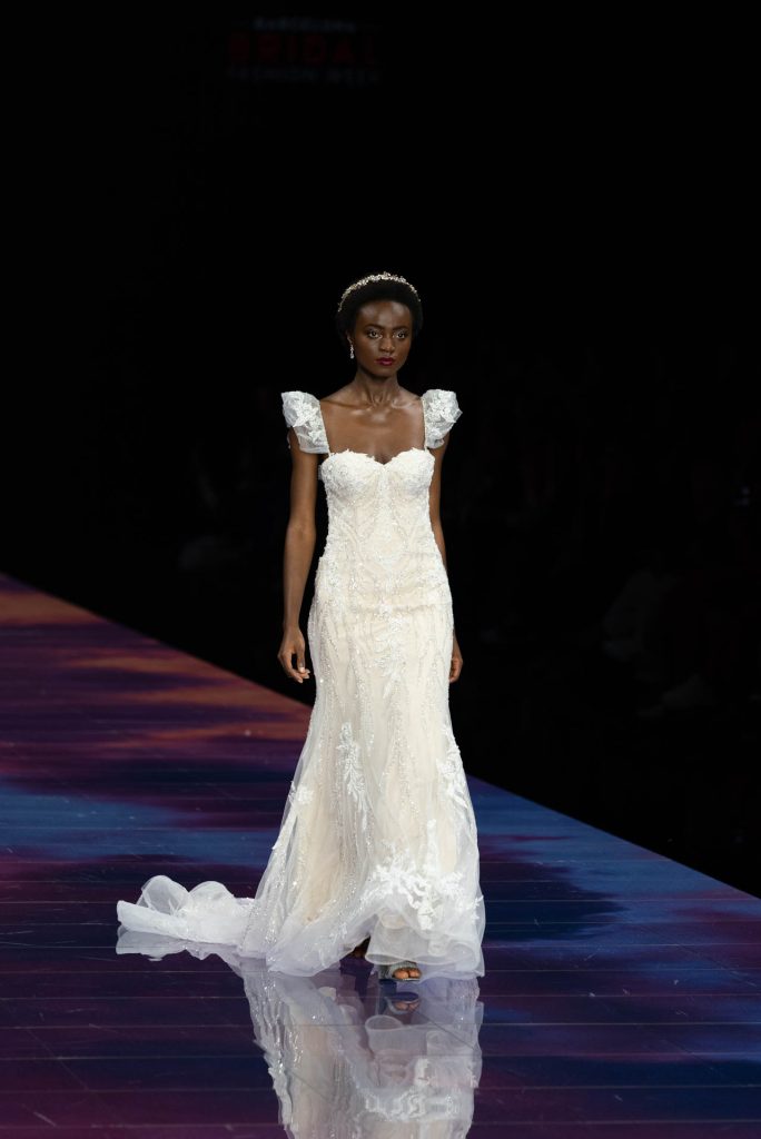 In questa immagine una modella indossa un abito da sposa Demetrios 2024 con ricami floreali in pizzo.