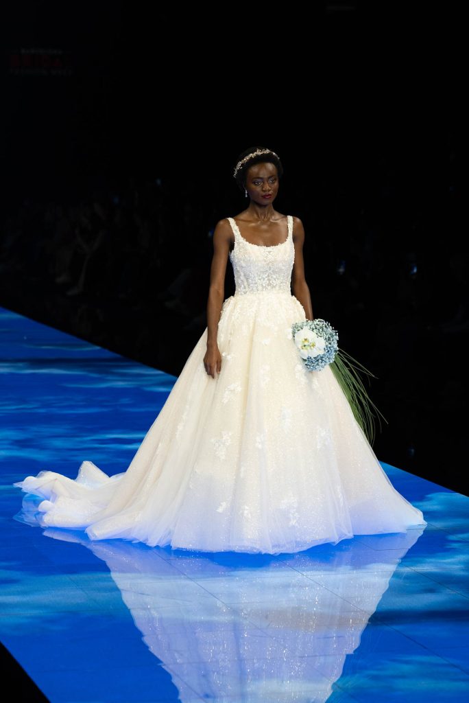 In questa immagine una modella indossa un abito da sposa Demetrios 2024 con ricami floreali in pizzo.