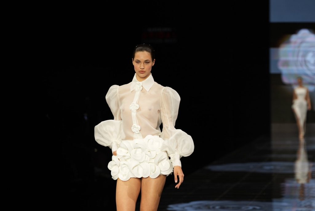 In questa immagine una modella indossa un abito da sposa Isabel Sanchis 2024 con camicia trasparente e minigonna con fiori in 3D. 