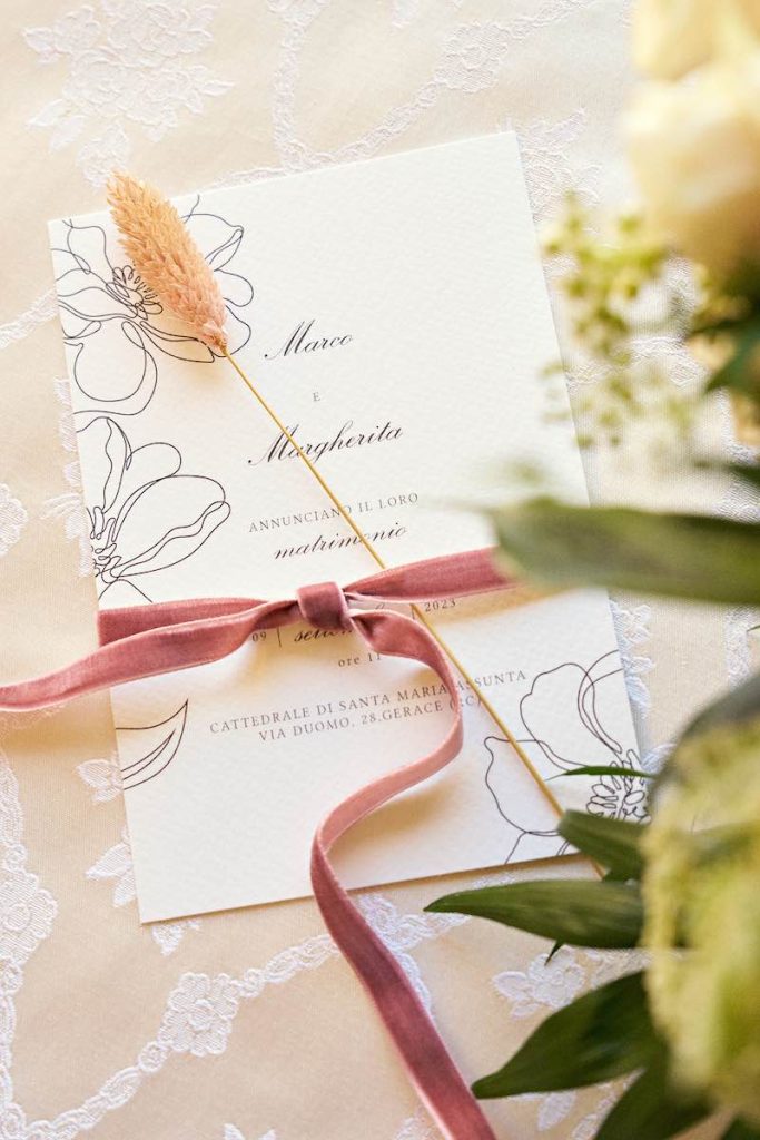 In questa foto una partecipazione di matrimonio calligrafica con nastro di velluto di colore rosa