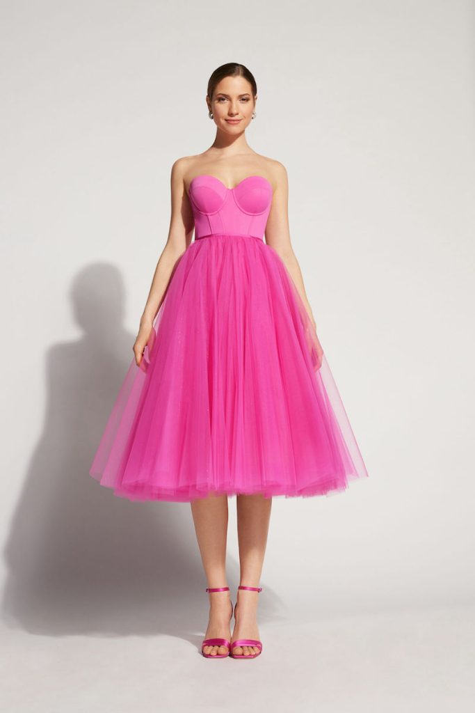 In questa foto una modella posa indossando un abito midi con gonna in tulle e corpetto a cuore di colore rosa per un look Barbiecore da cerimonia