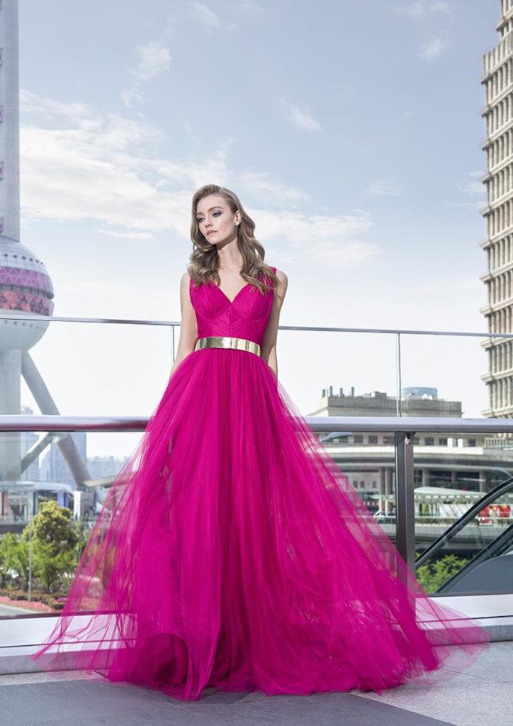 In questa foto una modella posa indossando un abito lungo in tulle di Pronovias di colore fucsia per un look Barbiecore da cerimonia