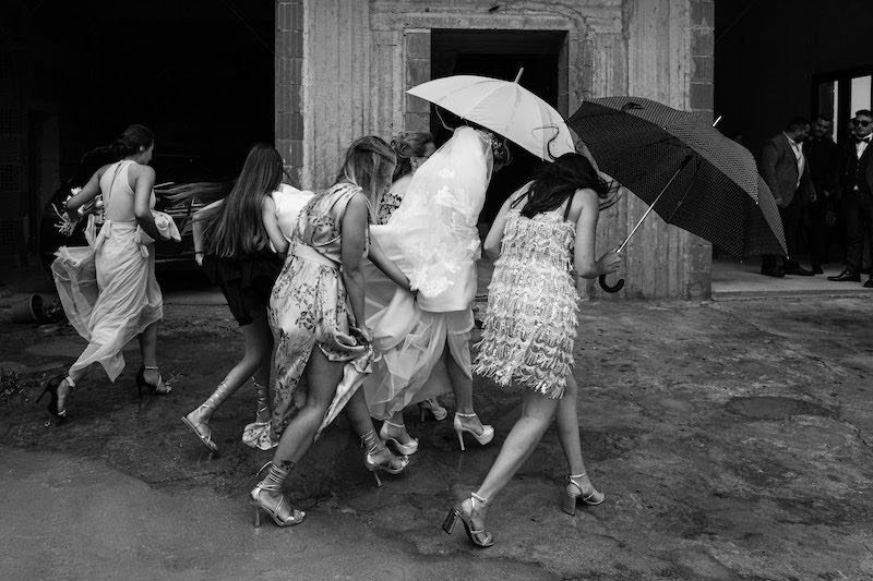 In questa foto in bianco e nero di Alberto Cosenza la sposa con le sue damigelle mentre si dirigono verso la chiesa del matrimonio camminando sotto agli ombrelli 