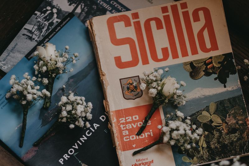 In questa foto alcuni opuscoli sulla Sicilia su cui sono poggiate le bottoniere composte da gypsophila e una piccola rosa bianche