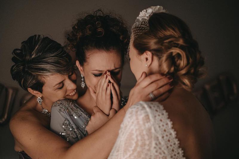 In questa foto di Alberto Cosenza una sposa di spalle mentre viene abbracciata dalle testimoni commosse