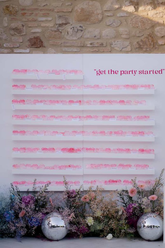 In questa foto un tableau de mariage con occhiali di colore rosa a forma di cuore stile Barbie di colore fucsia e rosa e la scritta "Get the party started"