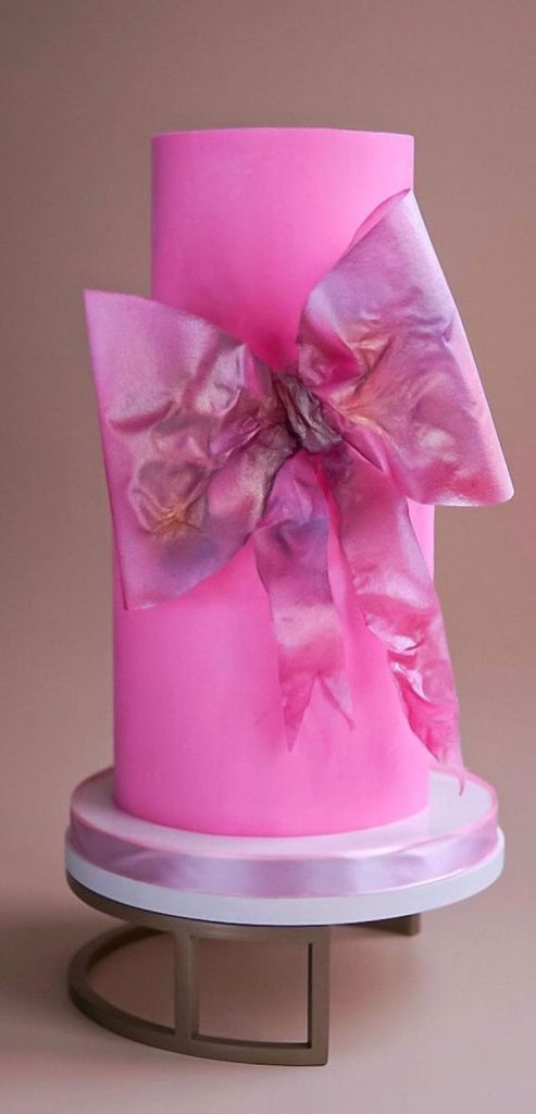 In questa foto una torta nuziale stile Barbie di colore fucsia con fiocco a tema 3D