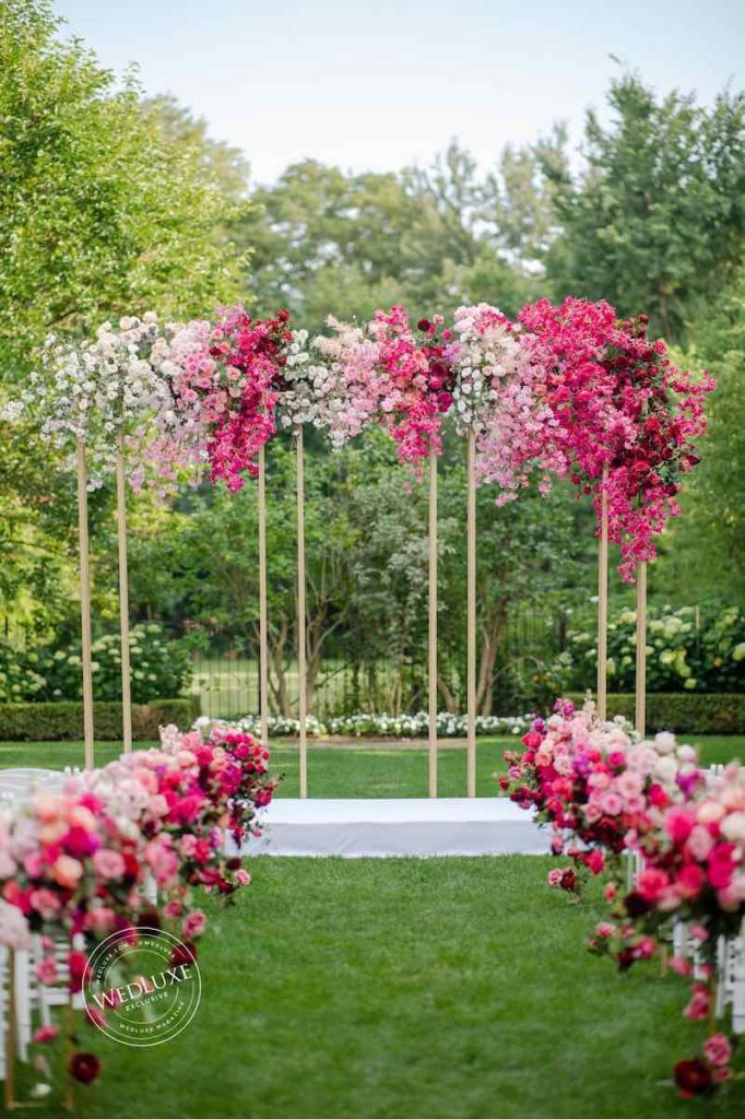 In questa foto l'allestimento di un matrimonio civile stile Barbie su un prato con decorazioni floreali di colore rosa, fucsia e bianco lungo il corridoio centrale e sulla struttura dell'altare 