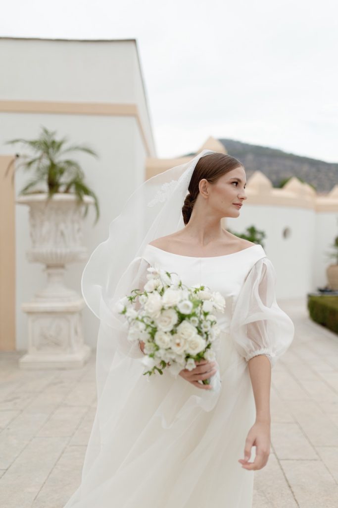 In questa foto una sposa sulla terrazza di Villa del Gattopardo mentre, rivolta alla sua sinistra, tiene in mano un bouquet di fiori bianchi