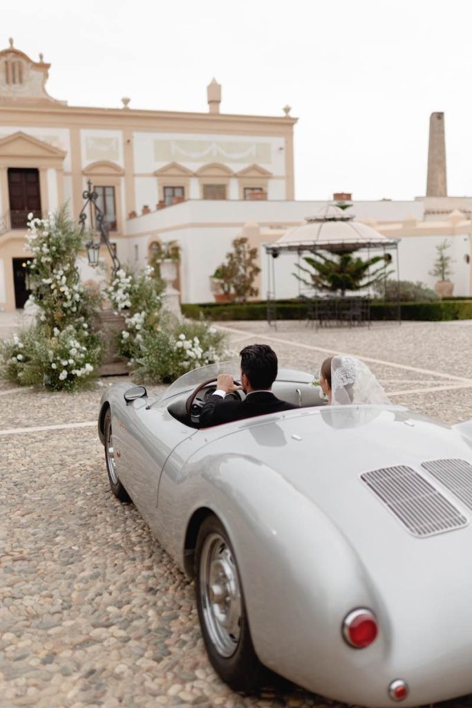 In questa foto due sposi a bordo di un'auto vintage all'arrivo al loro Destination Wedding a Villa del Gattopardo