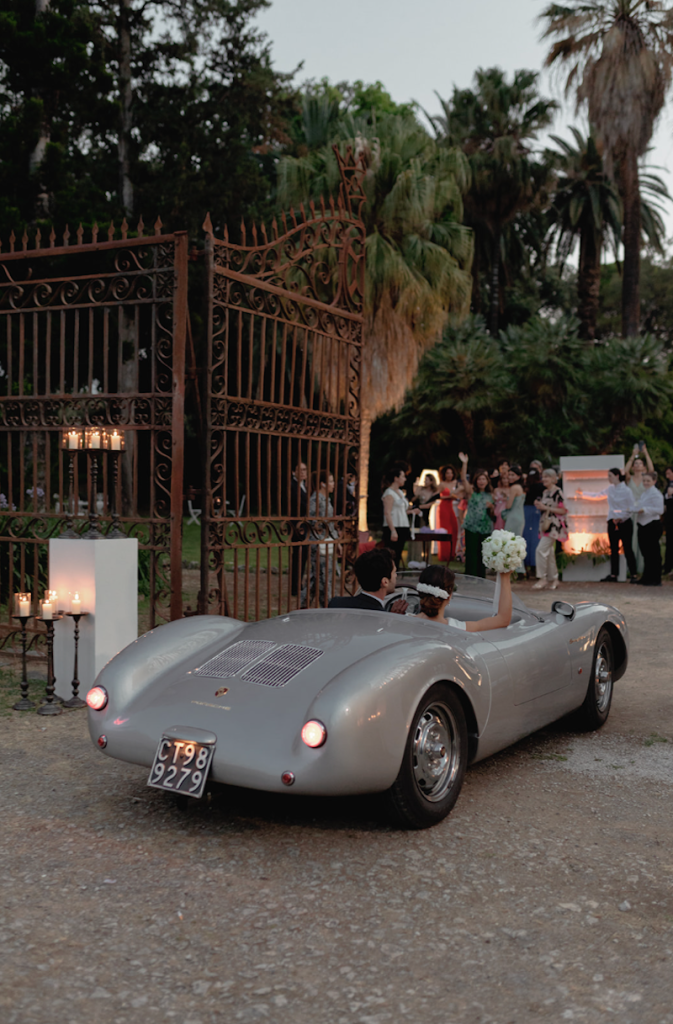 In questa foto gli sposi Elena e Nicola a bordo di una Porsche vintage grigio perla entrano nel giardino di Villa Tasca a Palermo