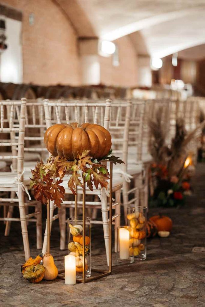 In questa foto il dettaglio dell'allestimento di un matrimonio simbolico in barricaia firmato da Erica Canova e realizzato nei toni dell'arancione con zucche, pampas e candele