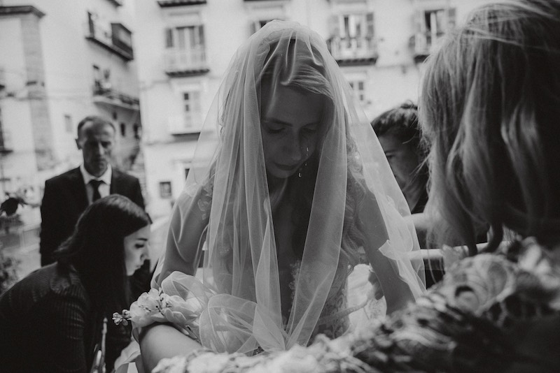 In questa foto in bianco e nero di Alessandro Tondo una sposa con la testa china verso il basso con il velo che le scende sul viso prima di entrare in chiesa 