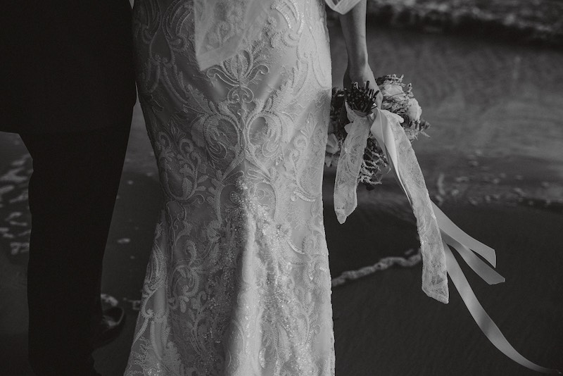 In questa foto in bianco e nero di Alessandro Tondo il dettaglio di una sposa che cammina sulla spiaggia mentre tiene il bouquet nella mano destra 